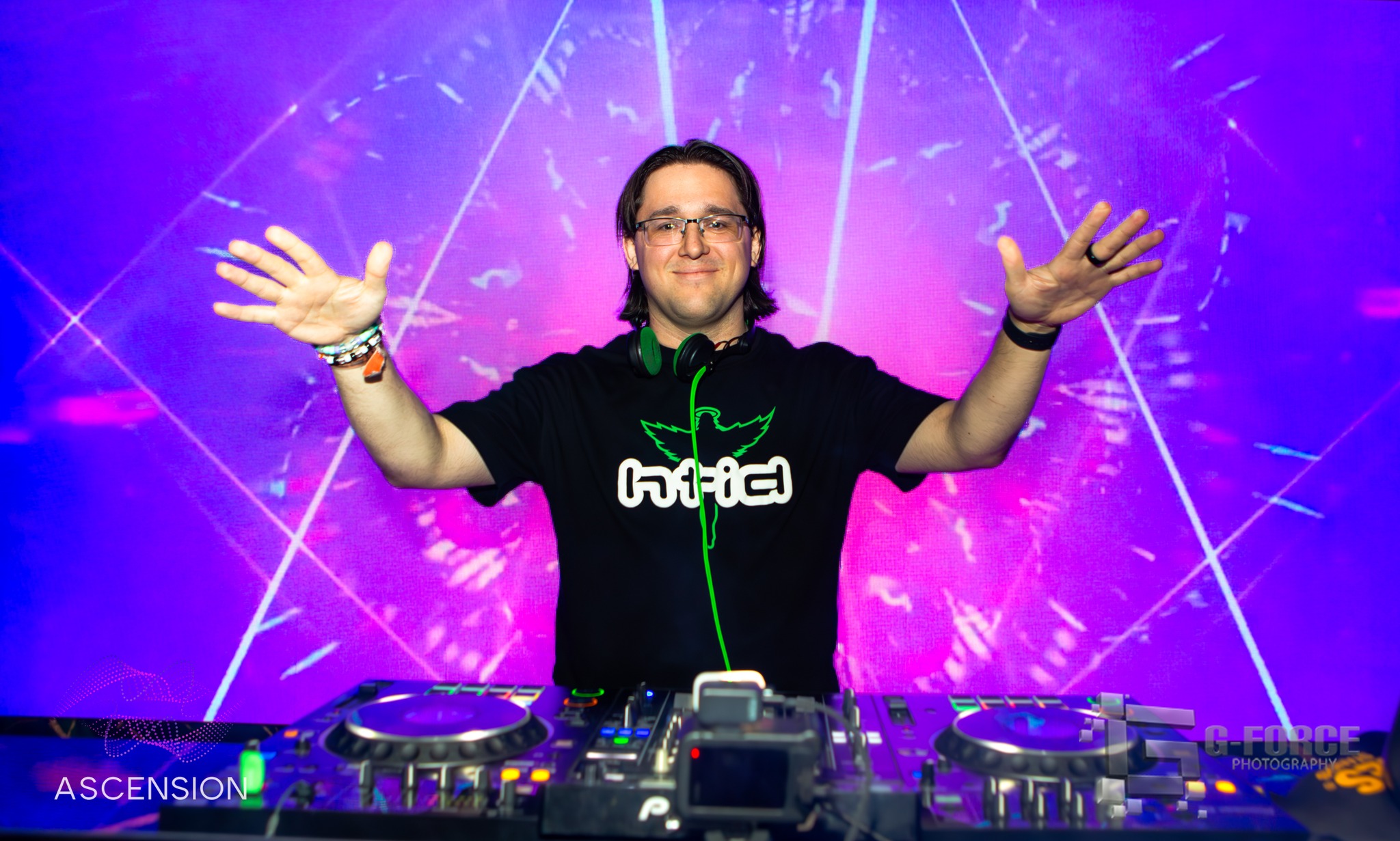 DJ with arms outstretched behind decks in front of a geometric LED backdrop